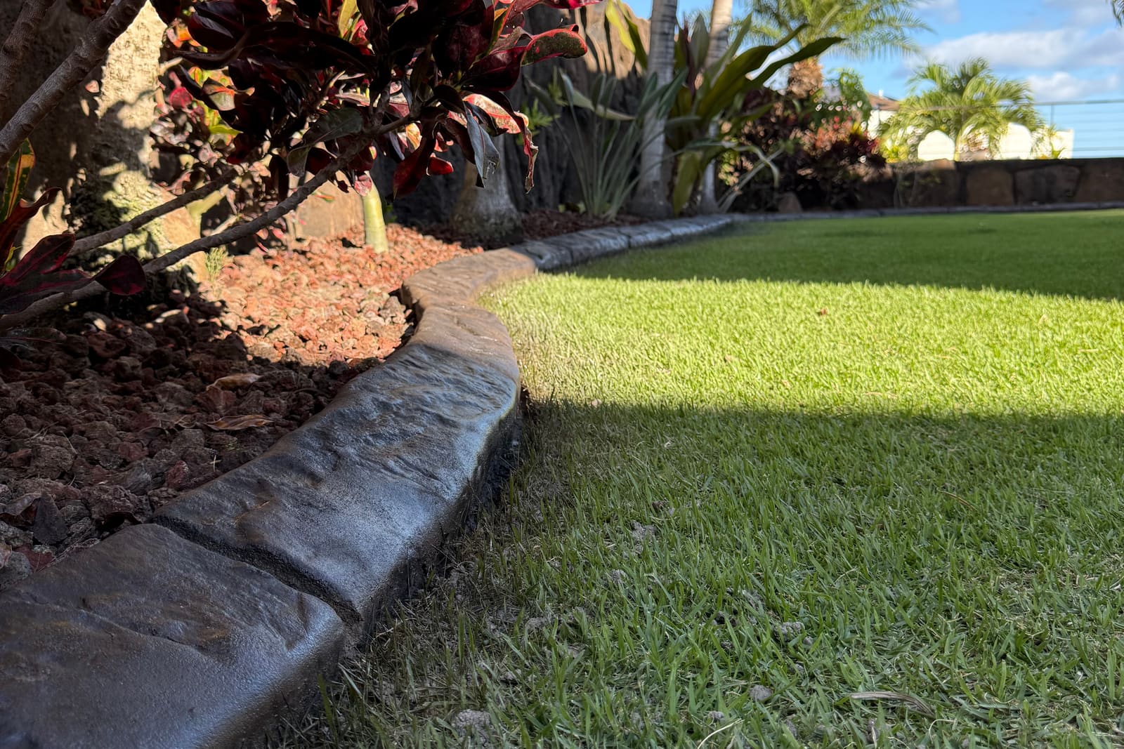 Hand-troweled concrete landscape curbing separating turf from a tropical planting bed